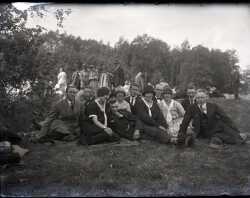 En grupp kvinnor och mn ligger och sitter p en grsmatta med flera mnniskor i bakgrunden. - klicka fr att frstora