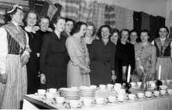 En grupp kvinnor under en vävkurs med vävar i bakgrunden och ett dukat kaffebord framför sig - klicka för att förstora