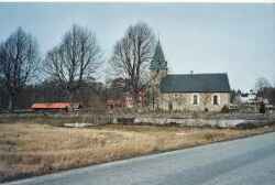 Edsbergs kyrka med gaveln på kyrkskolan till vänster och Höglunda gård till höger i bakgrunden - klicka för att förstora