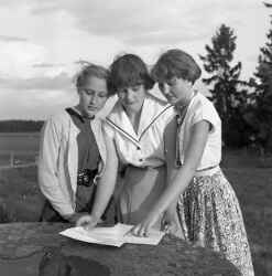 Tre kvinnor med ett papper på ett stenbord tillverkat av en kvarnsten. - klicka för att förstora