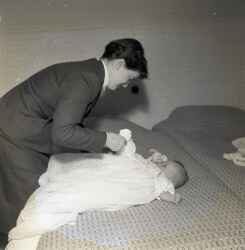 En kvinna med Hans Erik och Inger Rickardsson i Fjugestas barn på en säng i samband barnets dop - klicka för att förstora