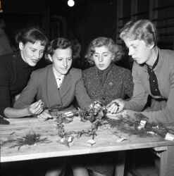 Fyra kvinnor vid ett bord med kransar på. Bilden ingår i en serie som även innehåller bilder från idrottstävlingar i Glanshammar som ska ha haft något med Uppsala att göra. - klicka för att förstora