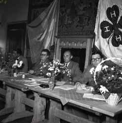 Fyra män vid ett bord i samband med JUFs riksstämma i Östersund. I bakgrunden hänger en svensk fana och fanan för 4H. - klicka för att förstora