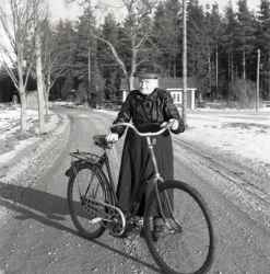 Äldre dam i mörk klänning med cykel. Bilden kan vara tagen längs vägen mellan Slästorp och Kvistbro stationssamhälle. - klicka för att förstora