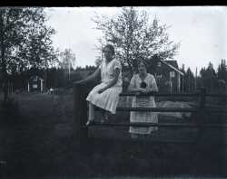 Tv kvinnor vid ett staket med en byggnaderna vid bondgrd i bakgrunden - klicka fr att frstora