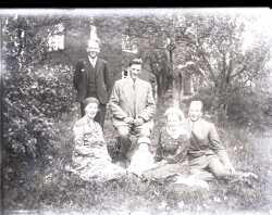 En pojke, ett barn, två kvinnor och två män på en gräsmatta med ett bostadshus i bakgrunden - klicka för att förstora