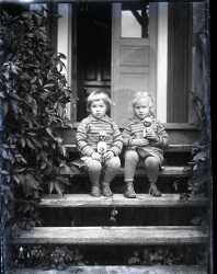 Två flickor med varsin docka på en trappa till ett bostadshus - klicka för att förstora
