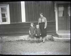 En kvinna med två barn framför ett hus - klicka för att förstora