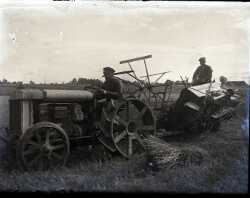 Två män på en traktor med järnhjul och en självbindare efter - klicka för att förstora