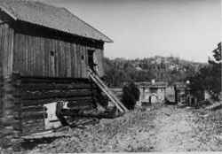 Klunkhyttan med bostadshus till h�ger och sj�lva mulltimmerhyttan till v�nster som �r under rivning - klicka f�r att f�rstora